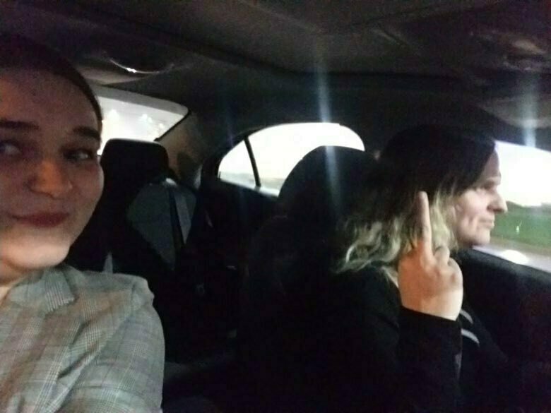 Nighttime selfie in a car: Kat smirks in the foreground while Zoey, at the wheel, raises a middle finger toward the camera